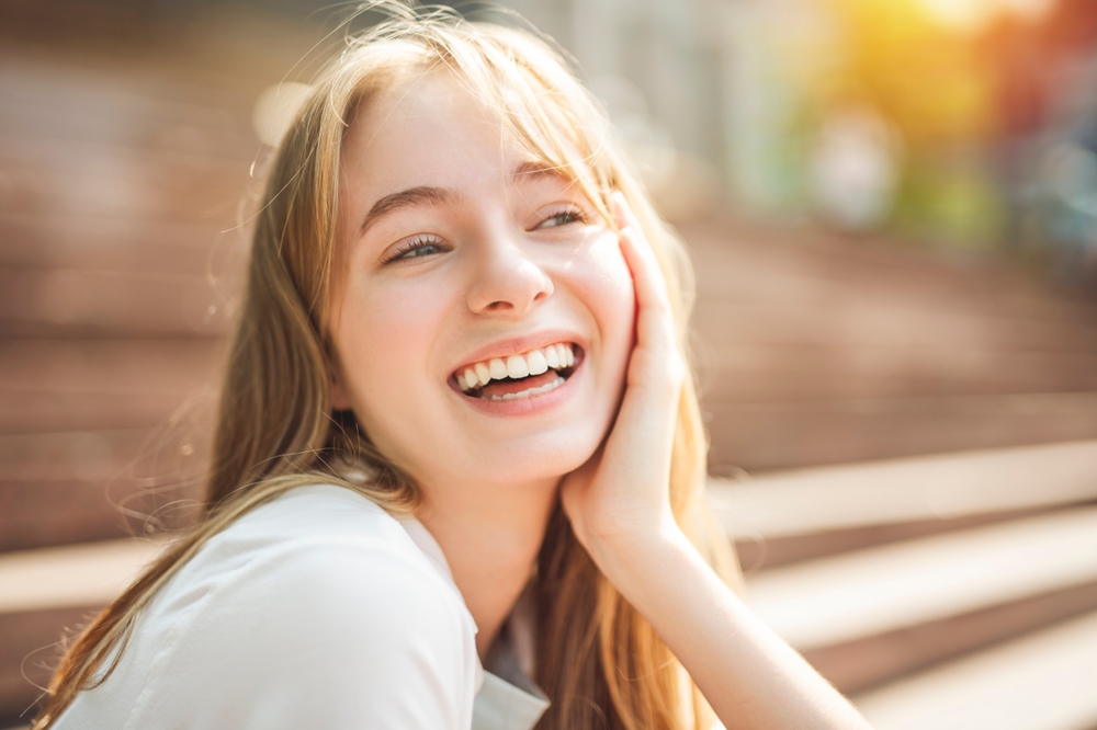 Happy woman with natural smile outdoors – Dental Implants in Arlington A cheerful young woman smiles under the sunlight, enjoying her renewed confidence and comfort after receiving professional dental implants – Dental Implants in Arlington.