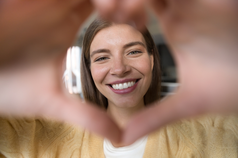 A cheerful woman frames her smile with a heart-shaped gesture, symbolizing confidence and gratitude after receiving compassionate emergency dental care – Emergency Dentistry.