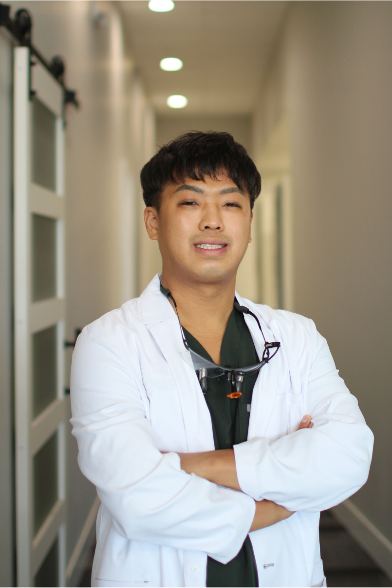 Dr. Jinyoung Jung, DDS professional portrait in dental office hallway – Dentist Arlington WA Smiling Dr. Jung Kim, DDS, wearing a white coat while standing in a bright dental office hallway – Dentist Arlington WA
